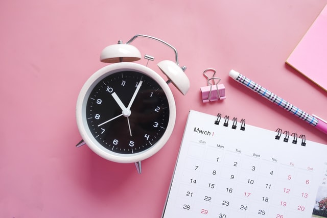 Alarm Clock, Stationery, Calendar, Pen, and Paper Clip on Pink Background